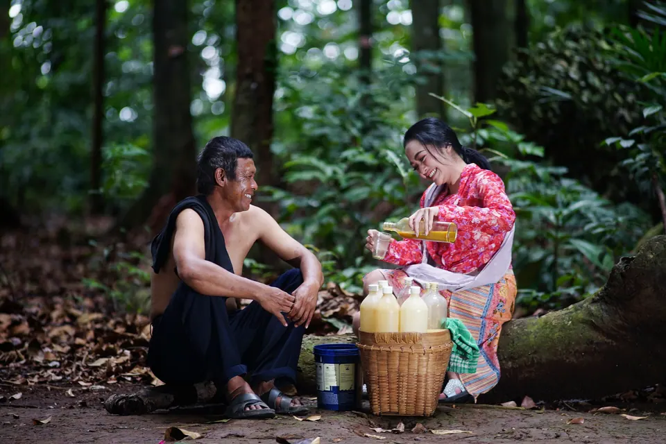 Penjual jamu gendong menuang jamu untuk pembeli di bawah pohon
